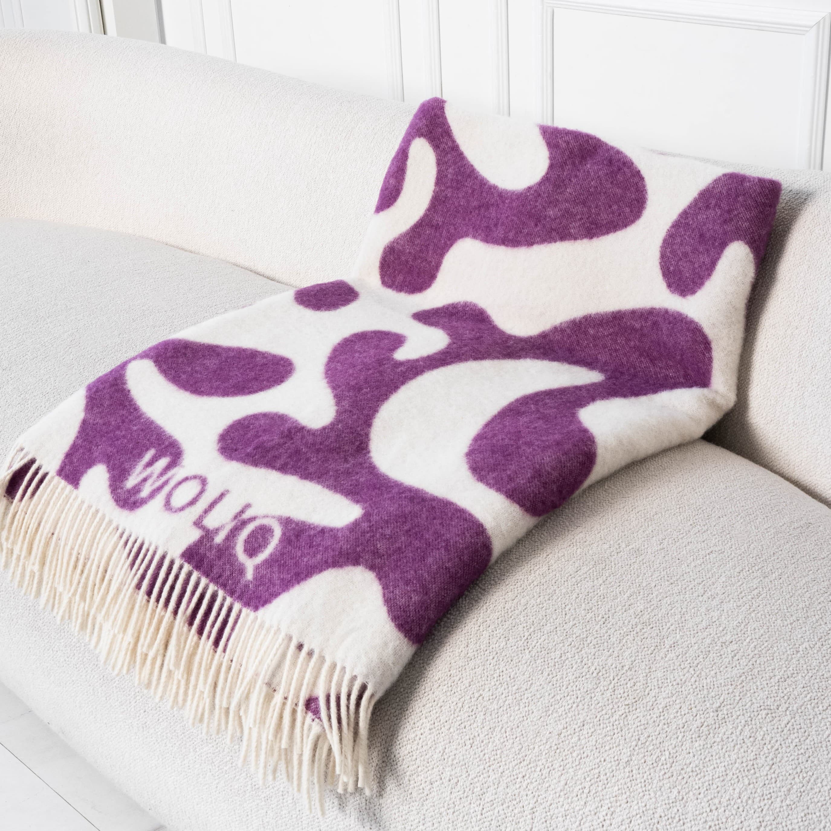 Violet and white curved flow wool blanket neatly placed on sofa – WOLIQ Calm Swirl