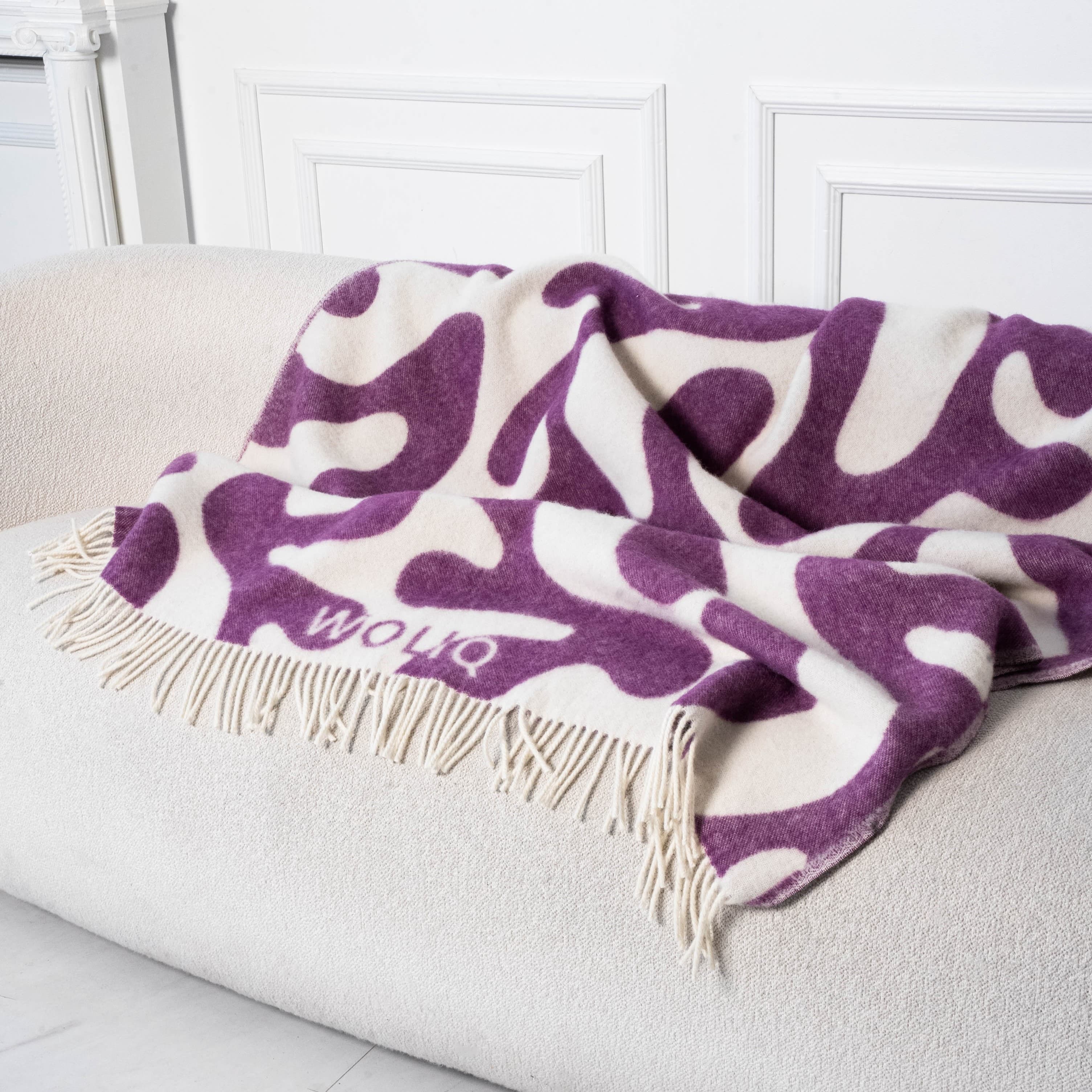 Violet and white curved flow wool blanket draped on sofa – WOLIQ Calm Swirl