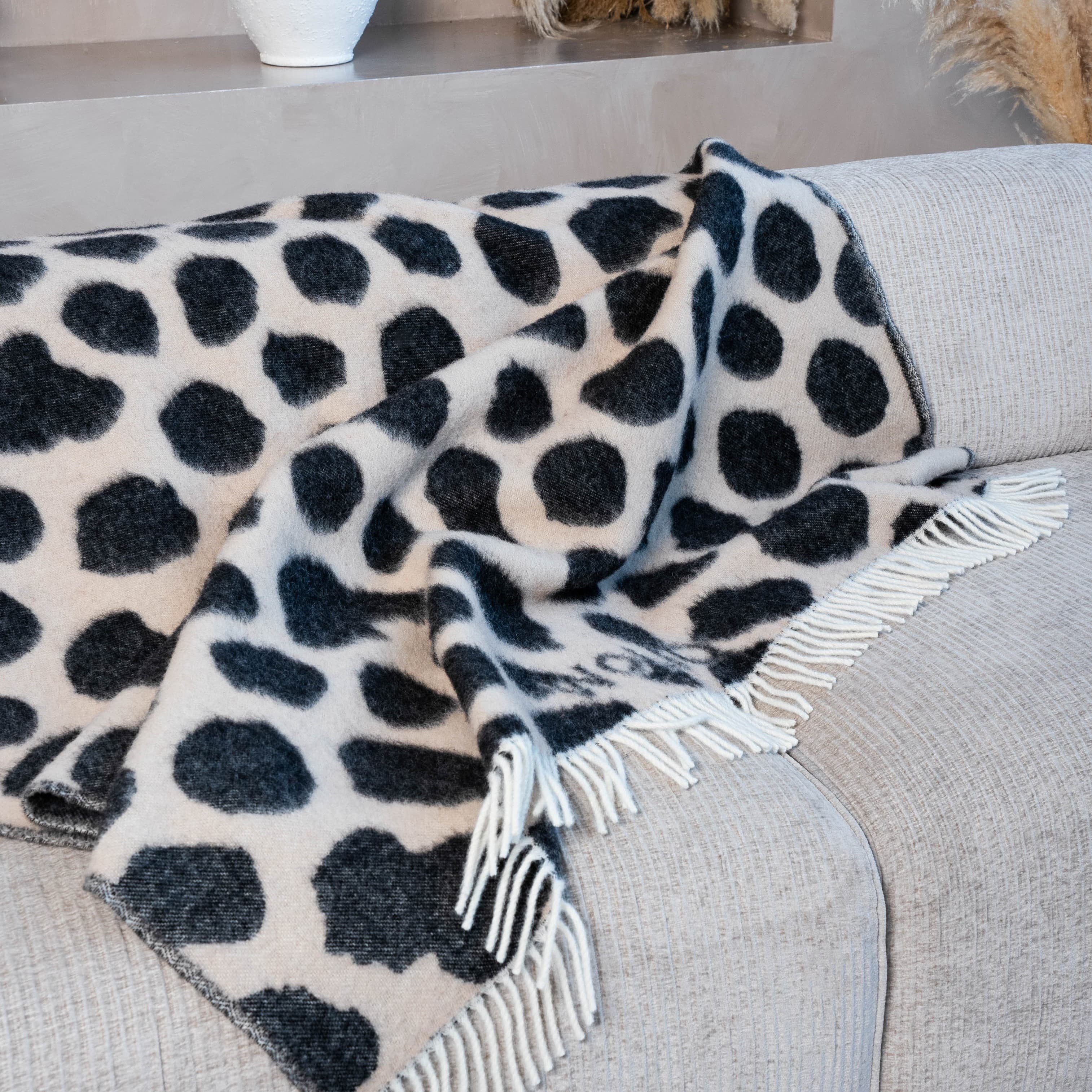Close-up of black and brown cow print wool blanket on sofa – WOLIQ Earthbound
