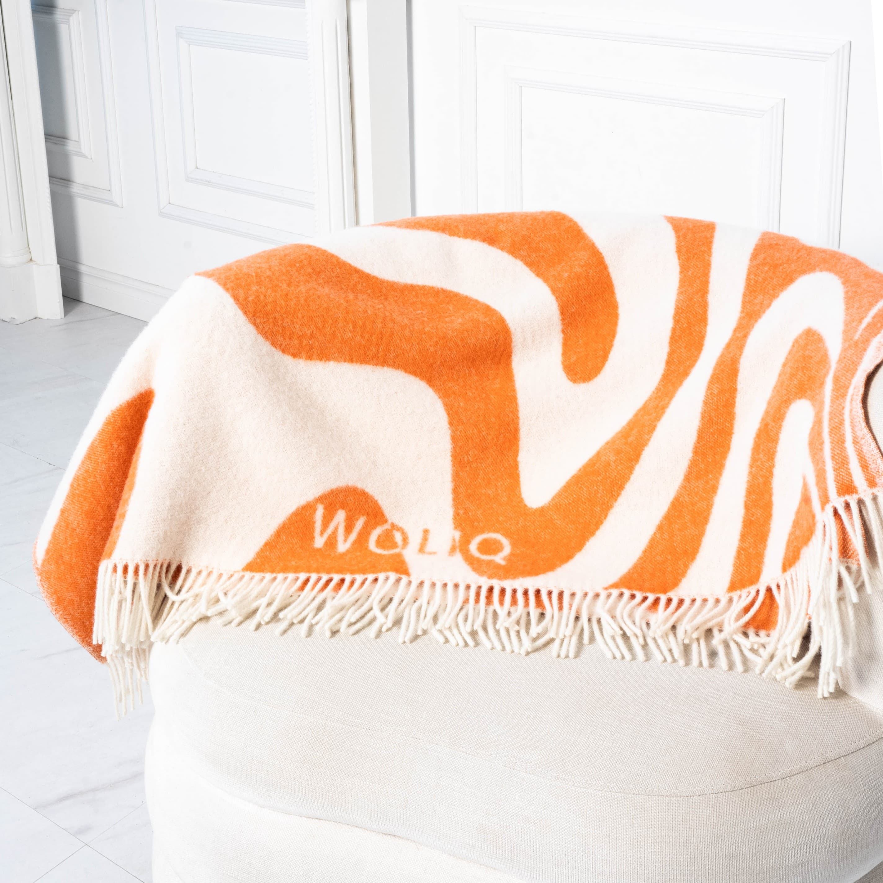 Orange and white flow pattern wool blanket neatly placed on sofa back – WOLIQ Flow Illusion