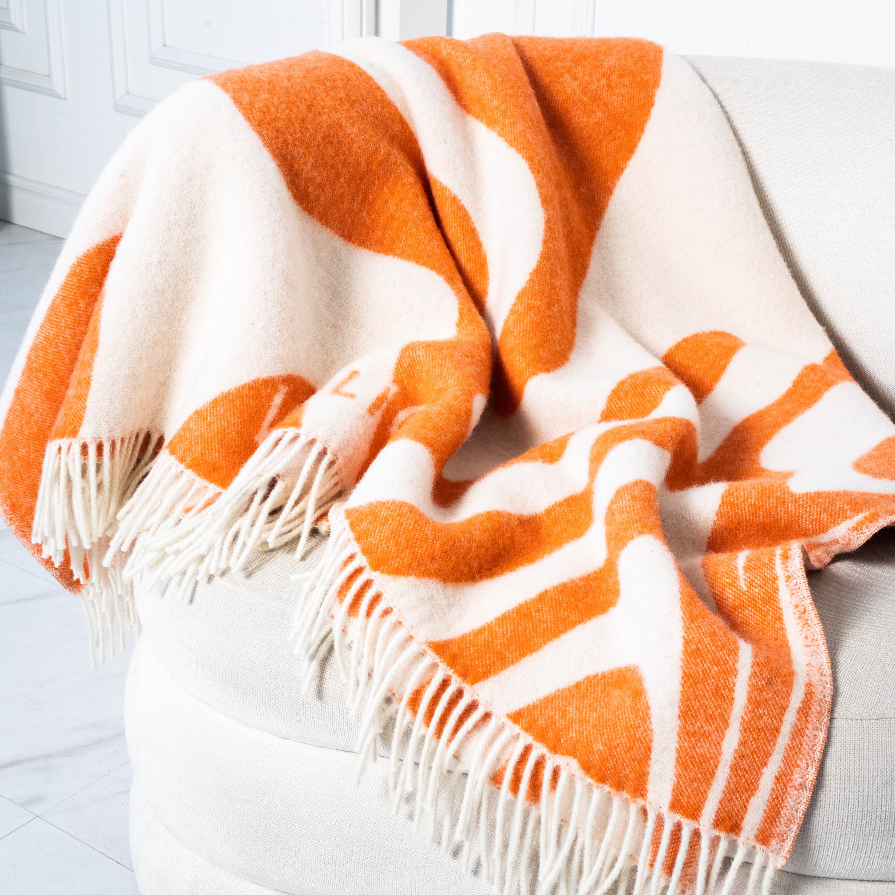 Close-up of orange and white flow pattern wool blanket on sofa – WOLIQ Flow Illusion