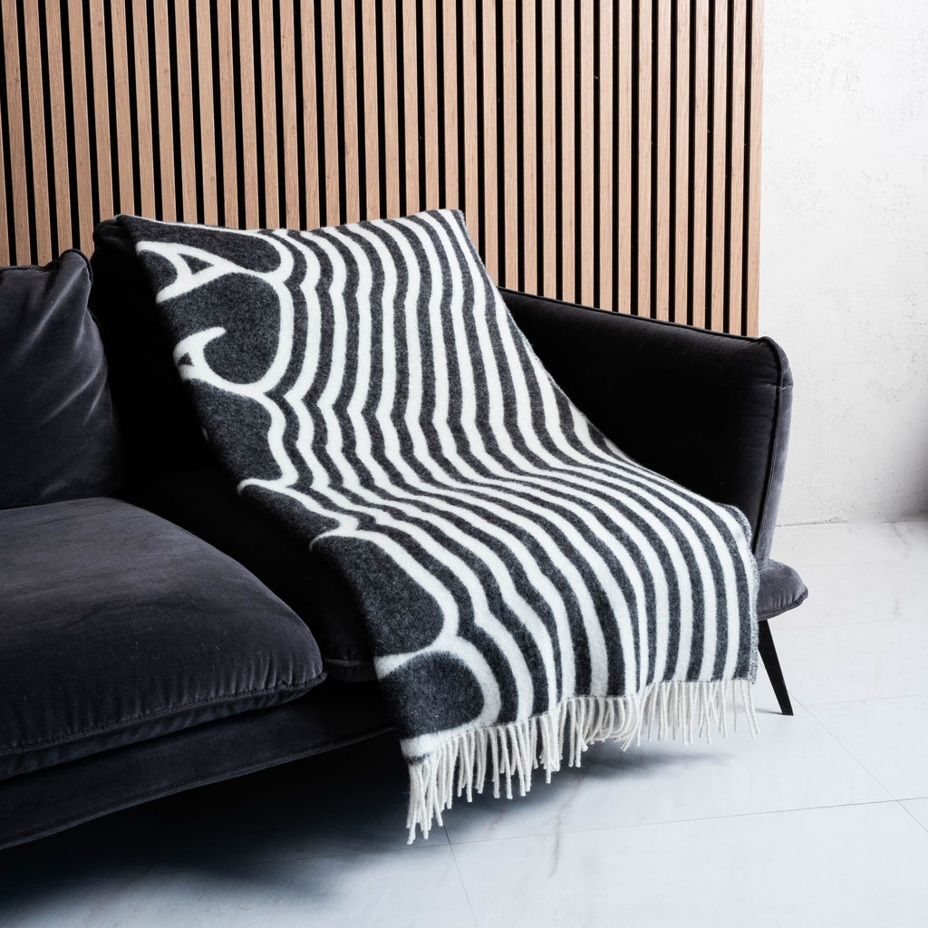 Black and white illusion text wool blanket neatly covering sofa with fringes visible – WOLIQ Illusion Wave