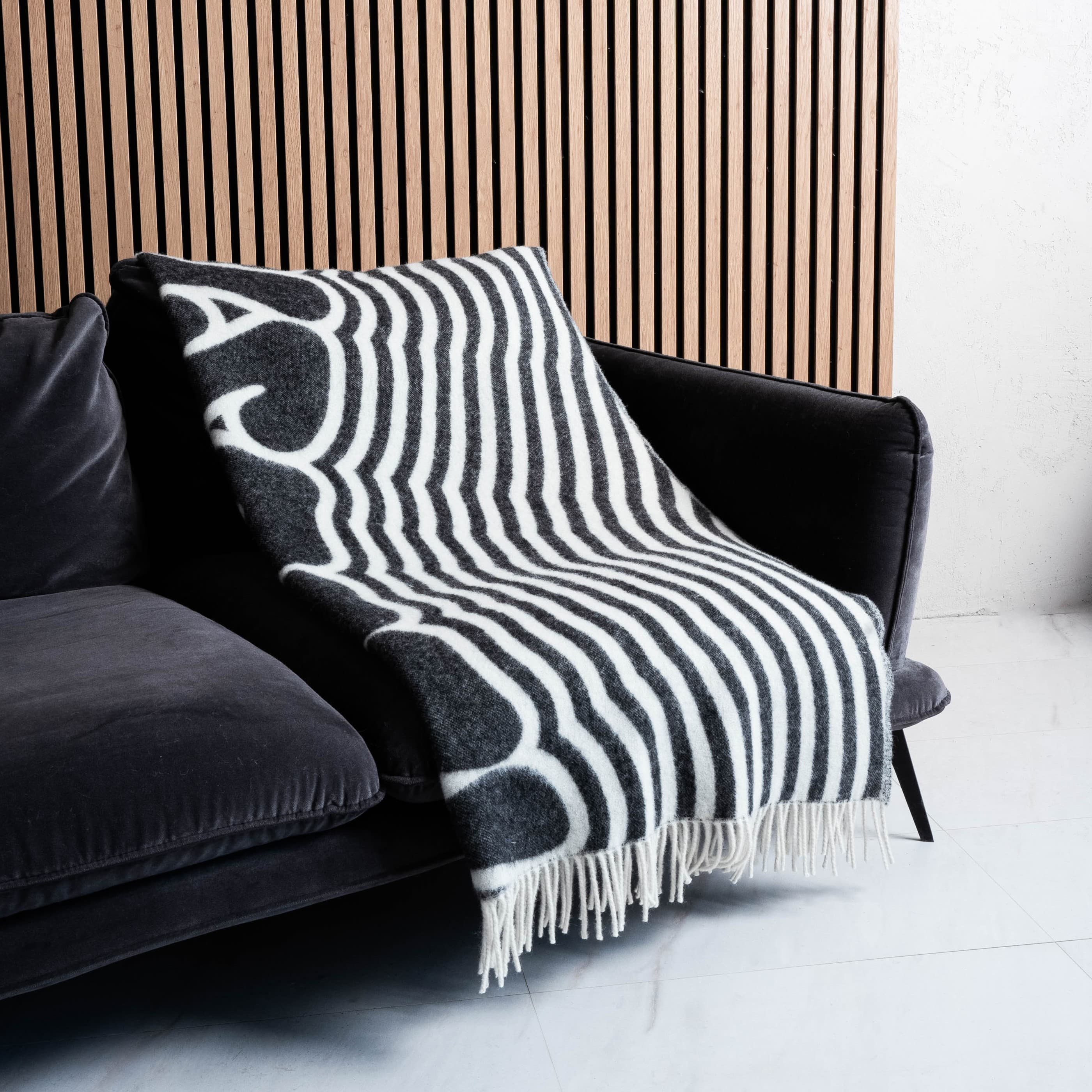 Black and white illusion text wool blanket neatly covering sofa with fringes visible – WOLIQ Illusion Wave