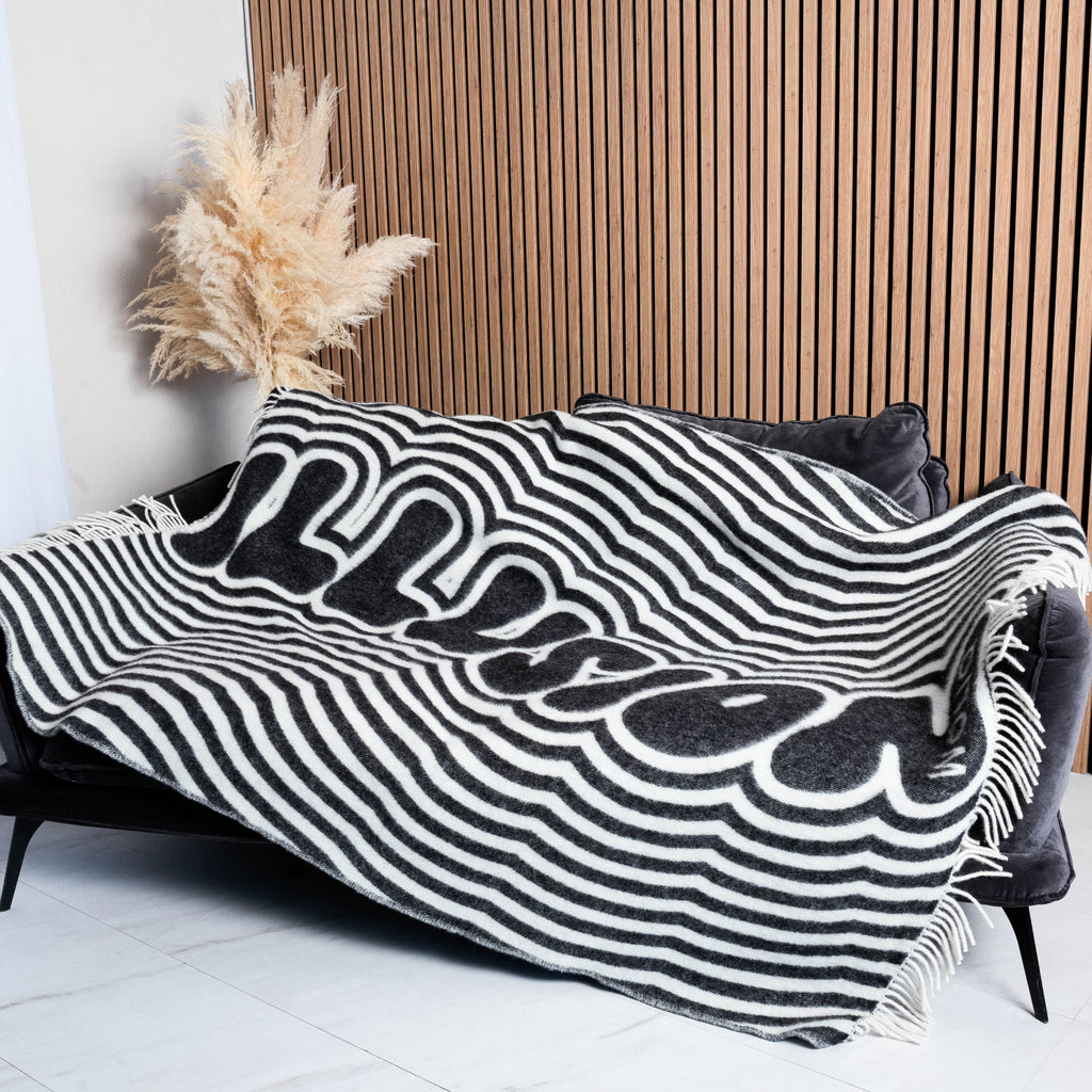 Black and white illusion text wool blanket draped on sofa – WOLIQ Illusion Wave