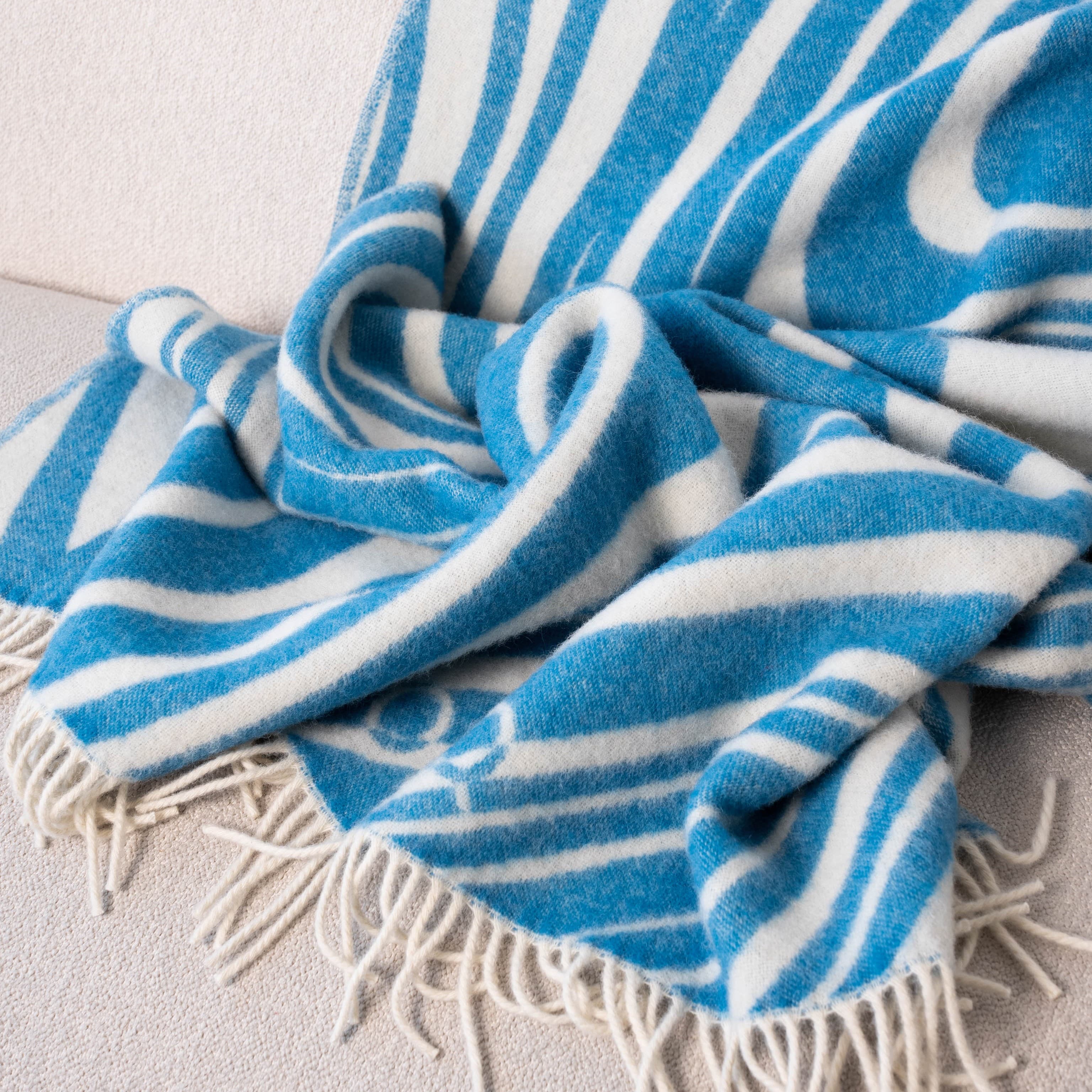 Close-up of blue and white wavy pattern wool blanket on sofa – WOLIQ Ocean Rhythm