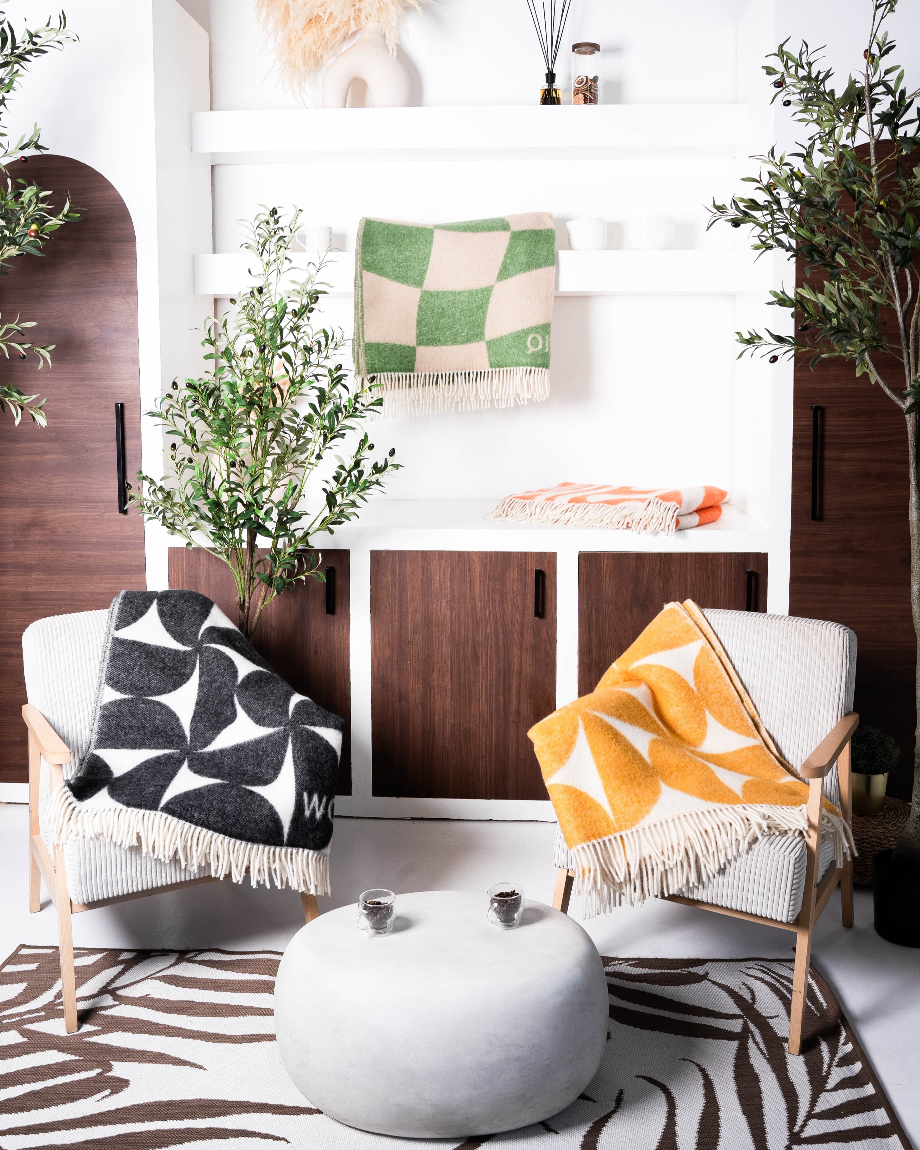 Four WOLIQ wool blankets in a natural interior setting with wood, greenery and soft neutral tones.