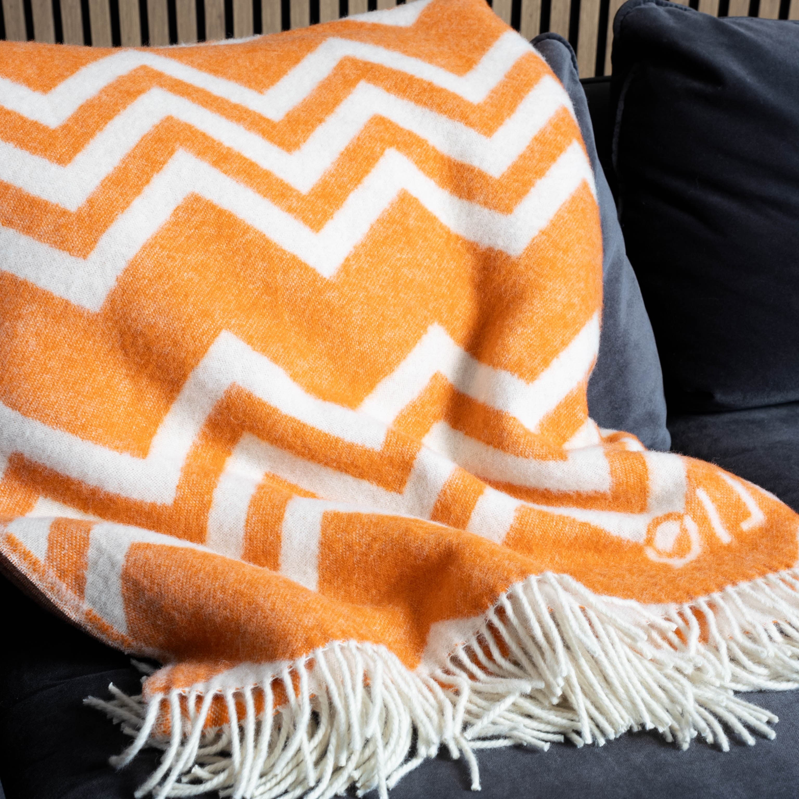 Close-up of orange and white zigzag wool blanket on sofa – WOLIQ Warm Glow